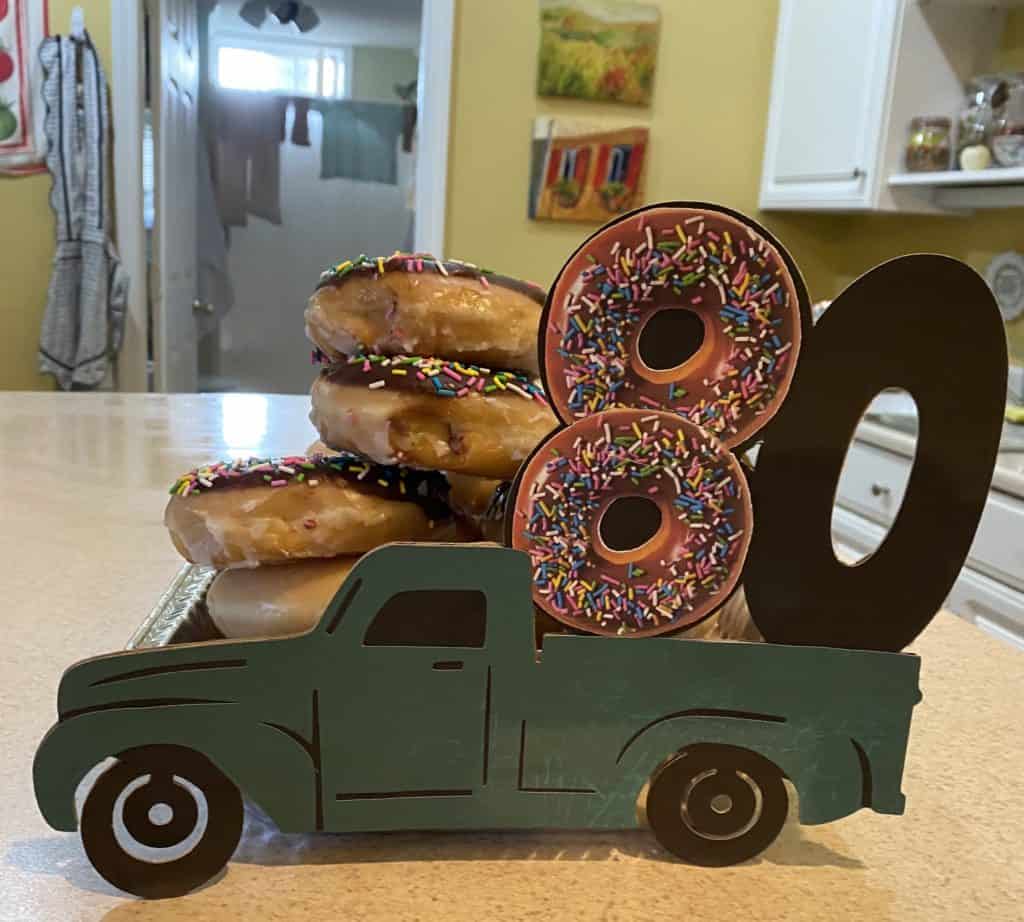 Truck with truck bed holding a large 80 with birthday donuts behind